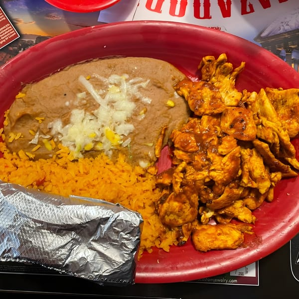 A red plate of Cazadores Mexican food with chicken, refried beans, rice, and a foil-wrapped item.