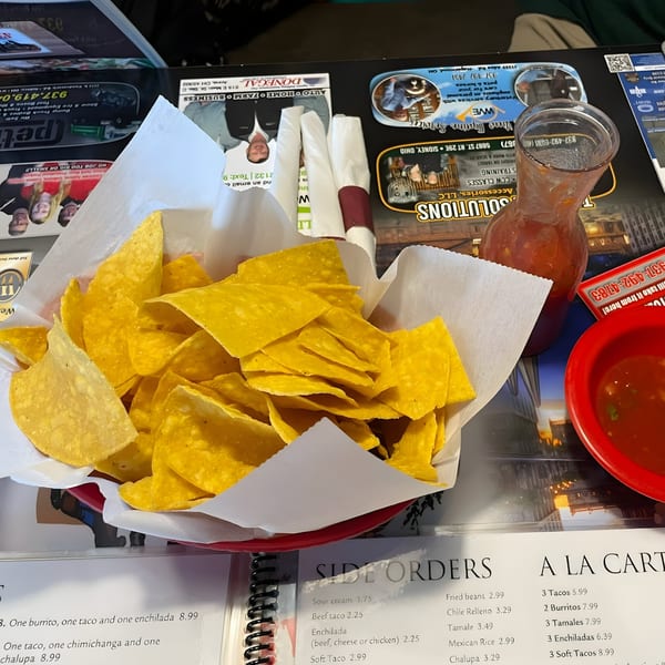 A basket of tortilla chips with a pitcher of salsa and a red bowl of salsa on a table.