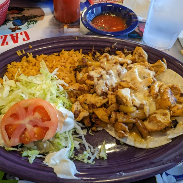 A purple plate of Cazadores Mexican Restaurant's chicken and rice, with lettuce, tomato, and sour cream.