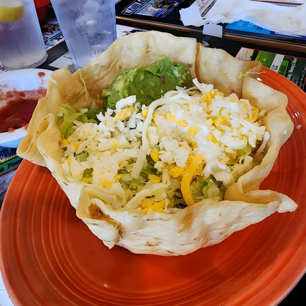 A large taco salad in a crispy tortilla bowl, topped with guacamole, lettuce, and shredded cheese.