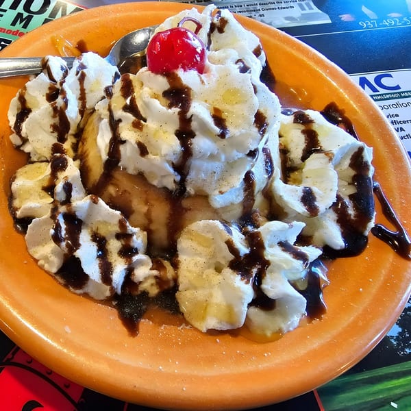 Fried ice cream dessert with whipped cream, chocolate syrup, and a cherry on an orange plate.