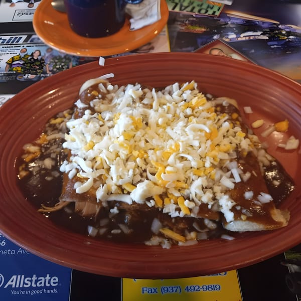 Cazadores Mexican Restaurant enchiladas covered in dark sauce, white and yellow shredded cheese, and diced onions.